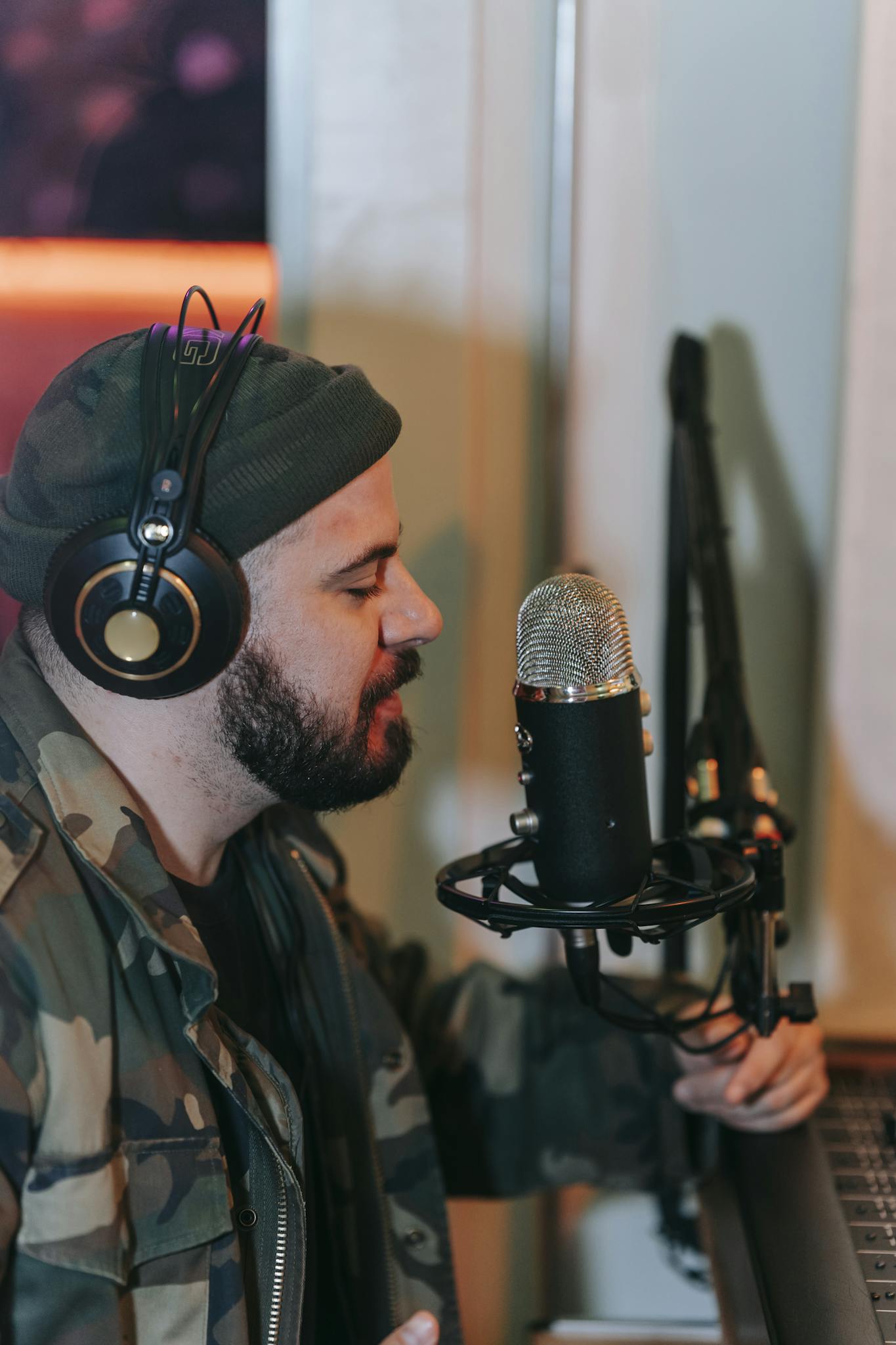 Man in headphones singing into a microphone in a home studio setting.